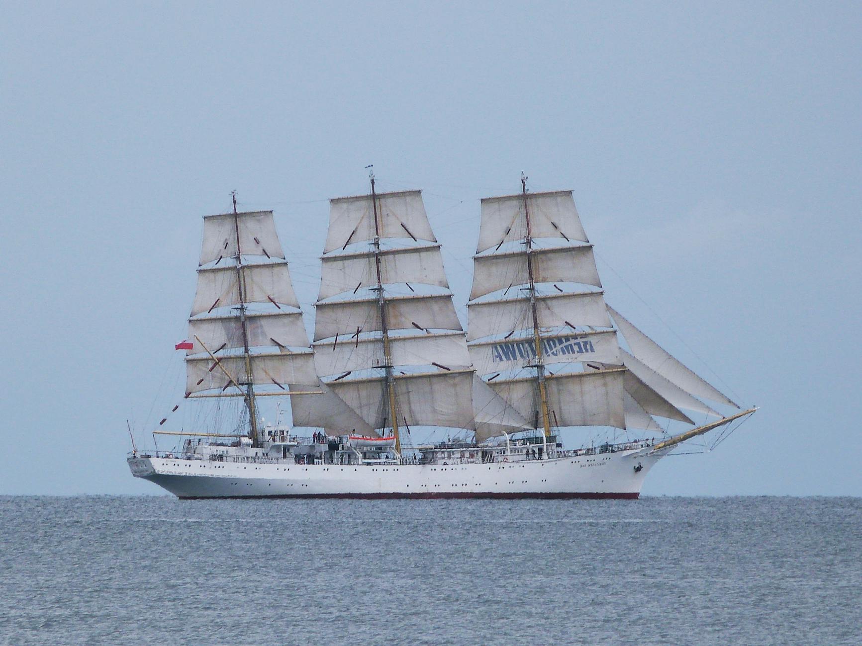Biały żaglowiec na pełnych żaglach płynie po spokojnym morzu