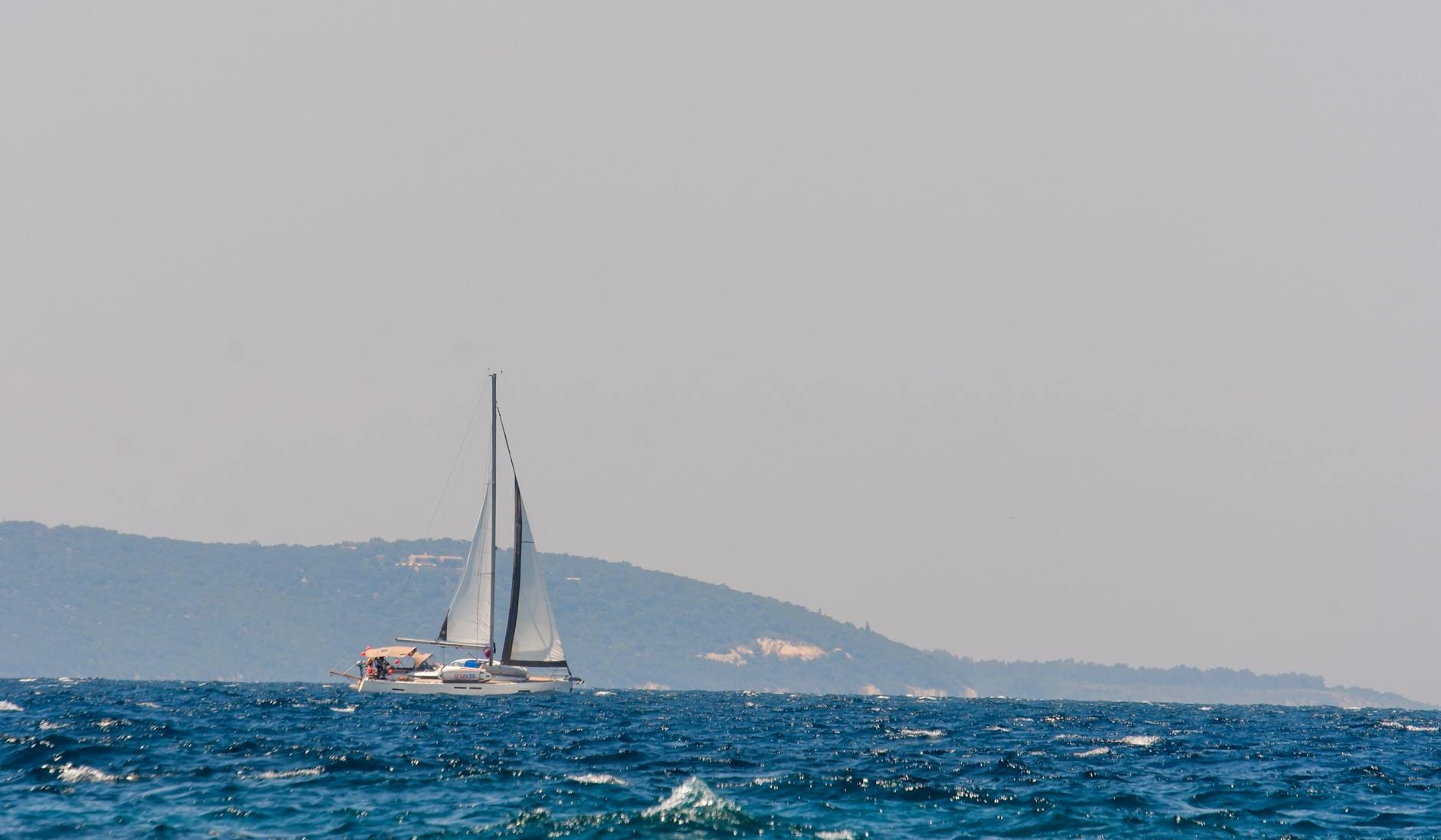 Jacht żaglowy płynie po spokojnym morzu przy słonecznym wybrzeżu