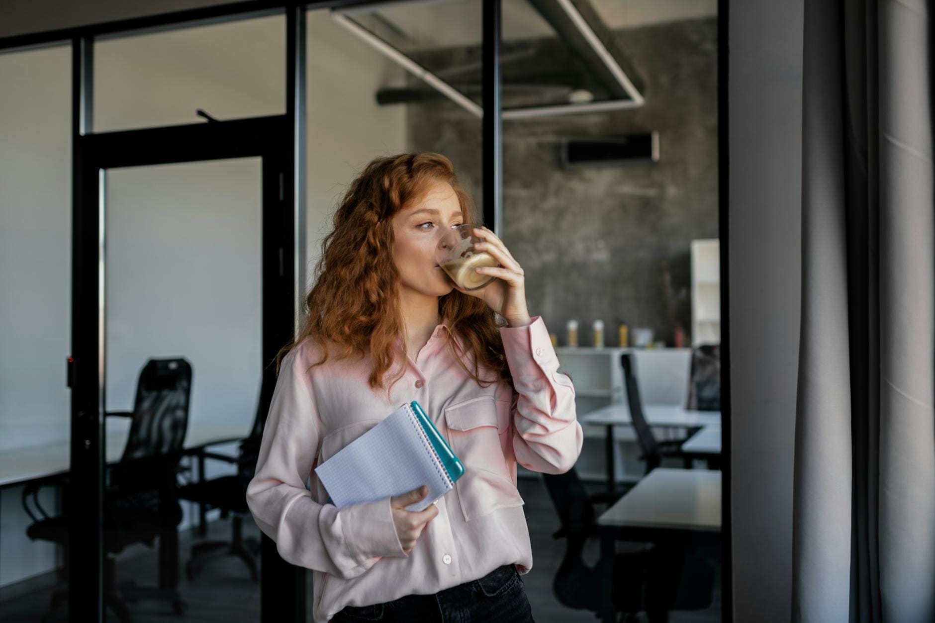 Rudowłosa pracowniczka pije kawę podczas przerwy w nowoczesnym biurze