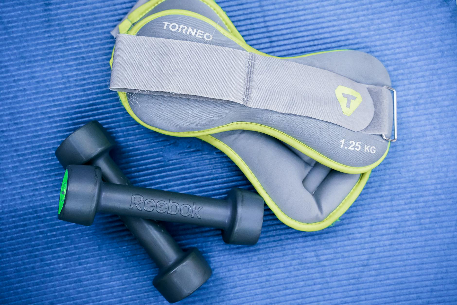 Hantle i obciążniki na kostki leżące na niebieskiej macie fitness
