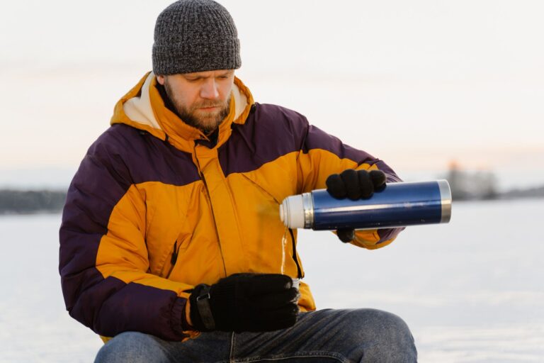 Mężczyzna zimą nalewa gorący napój z termosu w śnieżnym krajobrazie